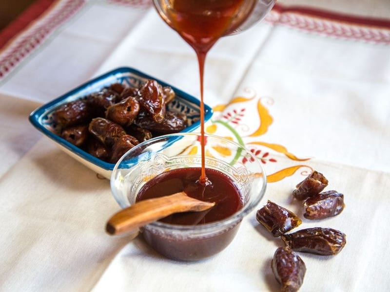 Amber date syrup being poured beside a dish of dates